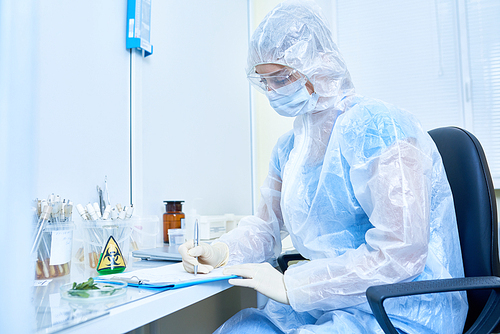 Side view portrait of female scientist wearing protective suit and mask working with hazardous materials in medical research laboratory