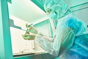 Side view portrait of unrecognizable female scientist wearing protective suit and mask working with plants in medical research laboratory