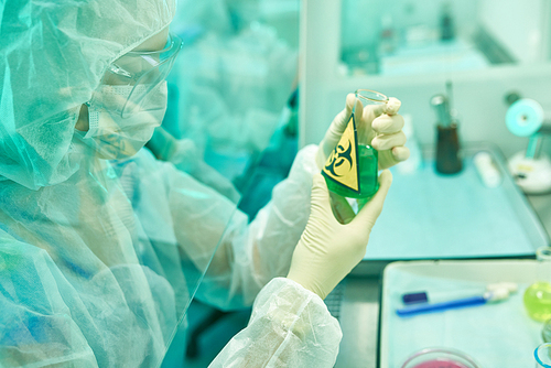 Side view portrait of unrecognizable female scientist wearing protective suit and mask working with biohazardous materials and viruses in medical research laboratory