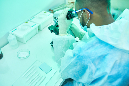 High angle portrait of young Middle-eastern scientist looking in microscope while working in laboratory doing medical research