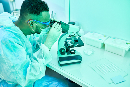 Side view portrait of young Middle-Eastern scientist using microscope while working in laboratory doing medical research