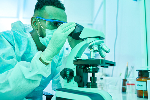 Side view portrait of young Middle-eastern scientist looking into microscope while working in laboratory doing medical research