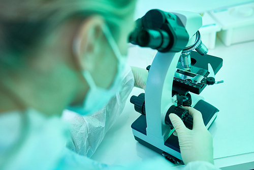 High angle portrait of young female scientist using microscope while working in laboratory doing medical research