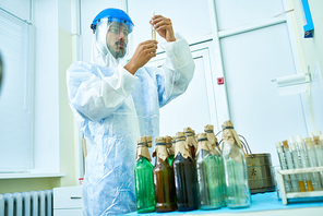 Low angle  portrait of young scientist wearing protective suit holding test tubes with hazardous materials while working in medical research laboratory