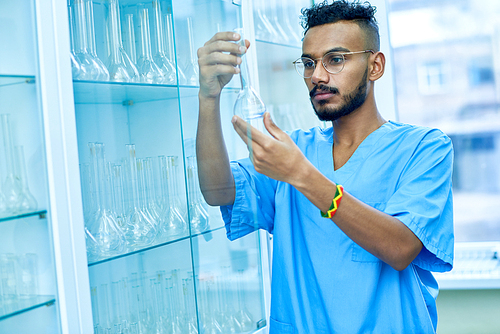 Portrait of young Middle-Eastern scientist holding test tube while checking glassware in medical research laboratory