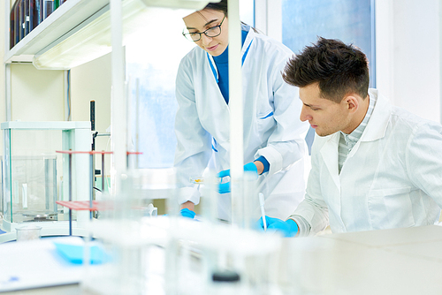 Group of talented young scientists wearing rubber gloves and white coats gathered together at modern laboratory and working on ambitious research