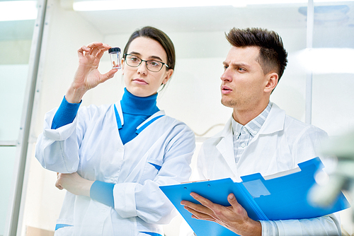 Group of talented young scientist discussing results of conducted experiment and taking necessary notes while gathered together in modern laboratory