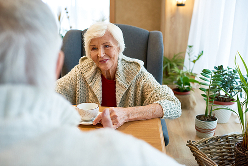 Portrait of pretty senior woman wearing knitted cardigan enjoying fragrant coffee while having romantic date in cozy small cafe