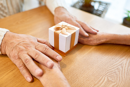 Loving senior couple holding hands while sitting at cafe table and exchanging Christmas presents, close-up shot