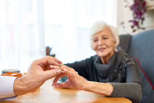 Unrecognizable senior man putting engagement ring on finger of his pretty soulmate while making marriage proposal at restaurant