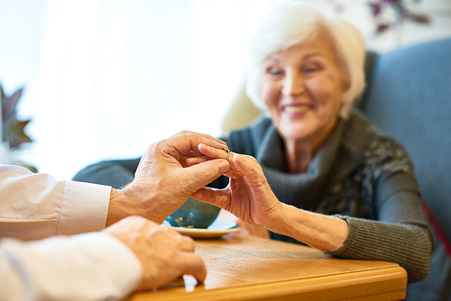 Receiving present for wedding anniversary: joyful senior woman looking at ring with toothy smile while her husband putting it on her finger