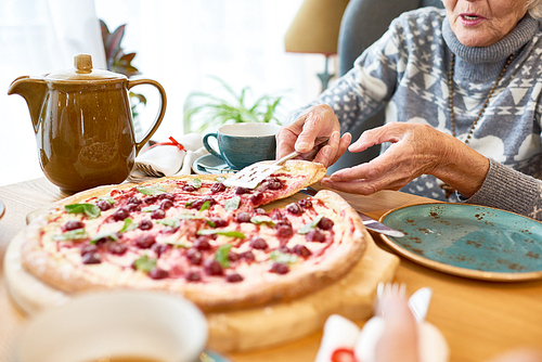 Close-up shot of unrecognizable elderly woman putting slice of appetizing dessert pizza on her plate while having tea party at home