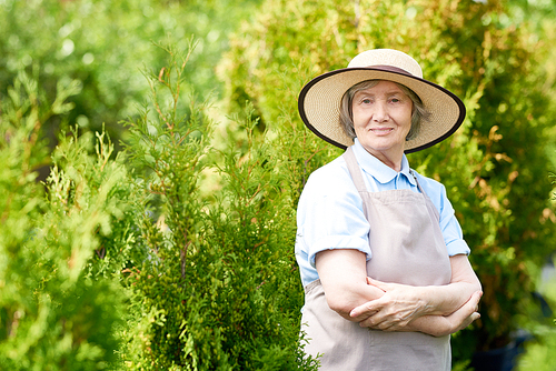 Portrait of smiling senior woman posing in garden standing with arms crossed and 