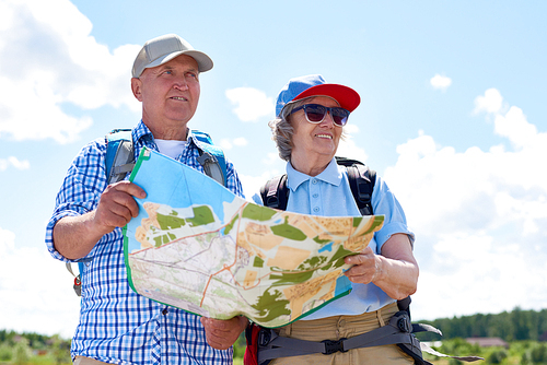 Waist up portrait of active senior couple travelling on hiking trip, stopping to look at map for directions against clear blue sky