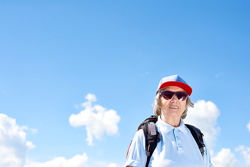Portrait of active senior woman travelling on hiking trip, posing smiling happily against clear blue sky, copy space
