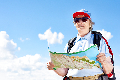 Portrait of active senior woman travelling on hiking trip, holding map smiling happily against clear blue sky, copy space