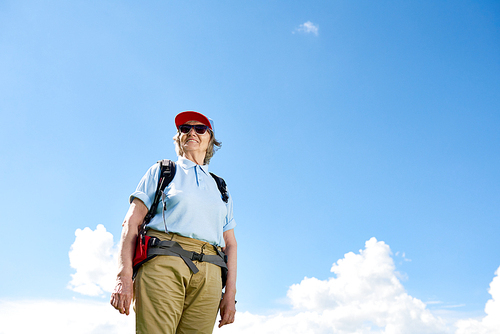 Low angle portrait of active senior woman travelling on hiking trip, posing smiling happily against clear blue sky, copy space