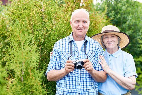 Portrait of senior couple taking pictures using photo camera on vacation in park