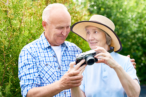 Waist up portrait of senior  couple taking pictures using photo camera on vacation in park