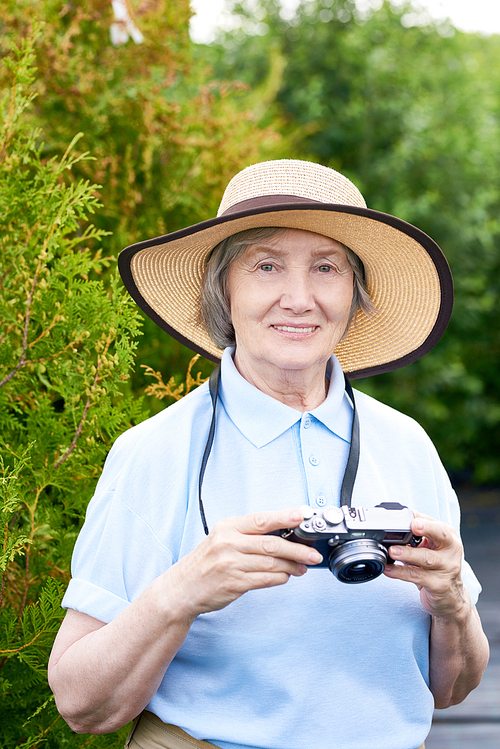 Waist up portrait of smiling senior woman  posing in park holding photo camera