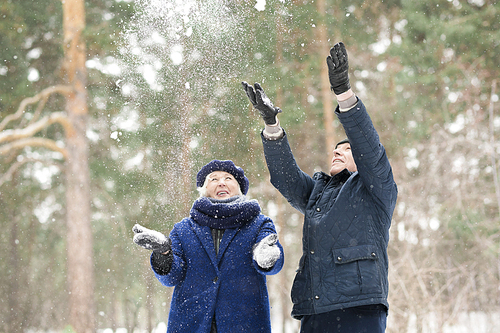 Waist up portrait  of carefree senior couple playing with snow in winter forest, copy space