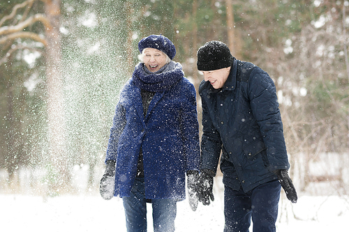 Waist up portrait  of excited senior couple playing with snow in winter forest and laughing happily, copy space