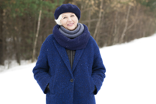 Waist up portrait of elegant senior woman posing in winter forest and smiling at camera, copy space