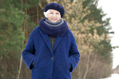 Waist up portrait of modern senior woman posing in winter forest and smiling at camera, copy space