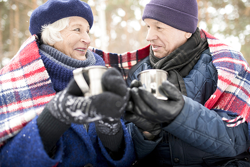 Low angle portrait of loving senior couple drinking hot cocoa outdoors in winter and sharing blanket looking in each others eyes