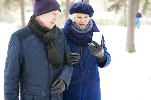 Waist up portrait of modern senior couple using smartphone while enjoying walk in winter forest