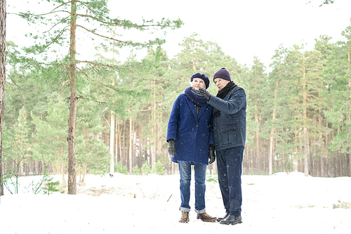 Full length portrait of senior couple taking break during walk in winter forest, copy space