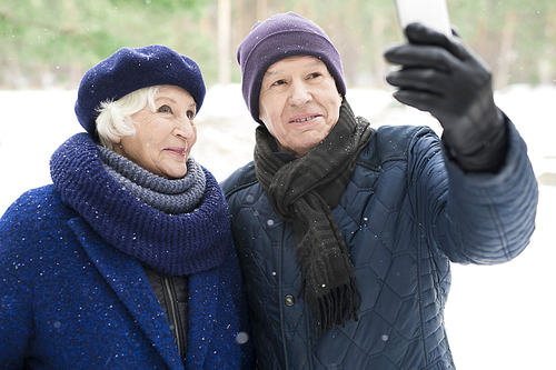 Portrait of modern senior couple taking selfie photo while enjoying walk in winter park