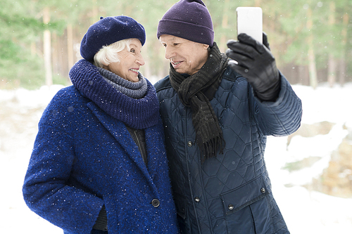 Waist up  portrait of loving senior couple taking selfie photo while enjoying walk in winter park