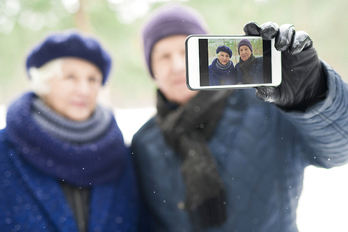 Blurred portrait of modern senior couple taking selfie photo during walk in winter, focus on image on screen, copy space