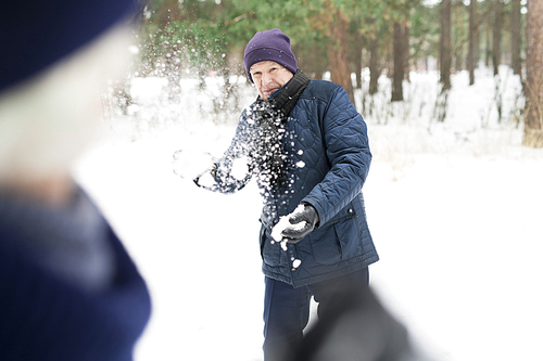 Portrait of active senior man playing snowball fight in winter forest, copy space