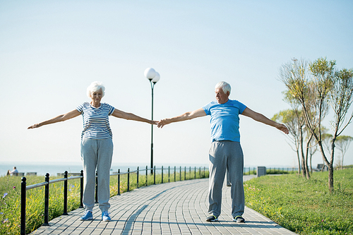 Full length portrait of active senior couple doing warm up exercises while standing on running track outdoors, copy space