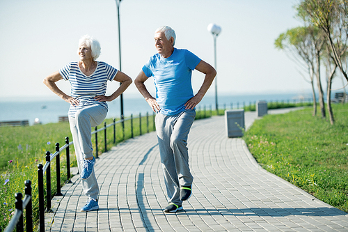 Full length portrait of active senior couple doing fitness exercises  standing on running track outdoors in sunlight looking happy, copy space
