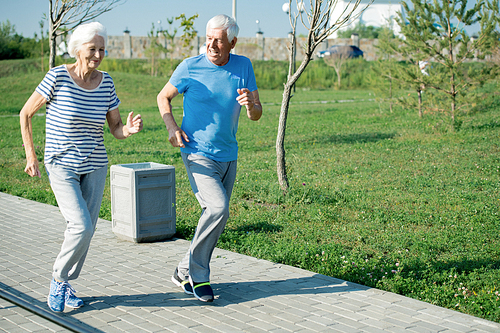 Full length portrait of active senior couple running on park lane outdoors , copy space