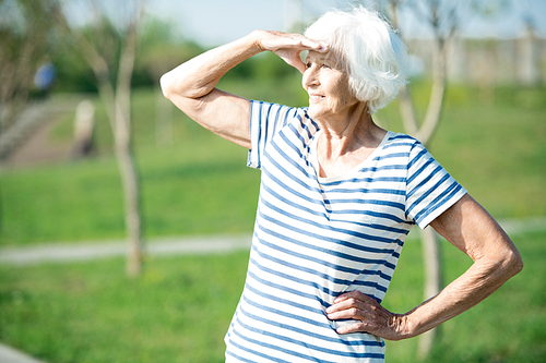 Waist up portrait of active senior woman looking away shielding eyes from sunlight outdoors, copy space