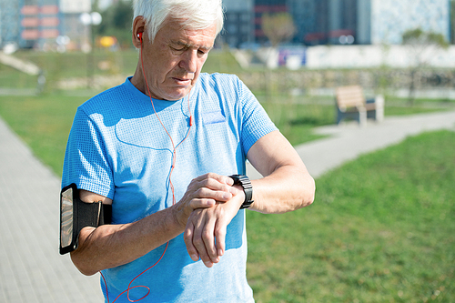 Waist up portrait of modern senior man setting up smart watch and listening to music while doing morning run in park, copy space