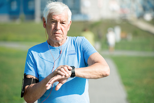 Waist up portrait of modern senior man setting up smart watch and listening to music in earphones  while doing morning run in park, copy space