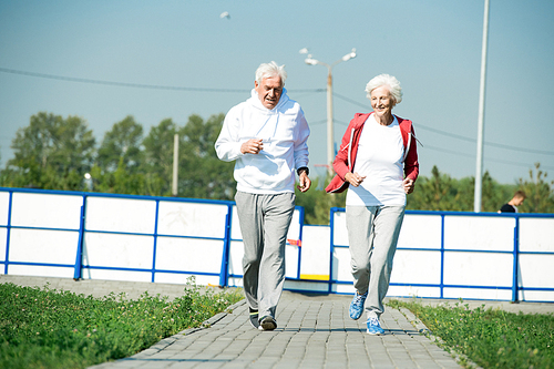 Full length portrait of active senior couple enjoying morning run outdoors in sunlight, copy space