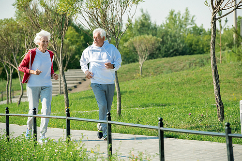 Full length portrait of active senior couple running in park and smiling happily in sunlight, copy space