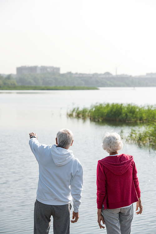 Rear view portrait of active senior couple standing by lake  together during walk, copy space