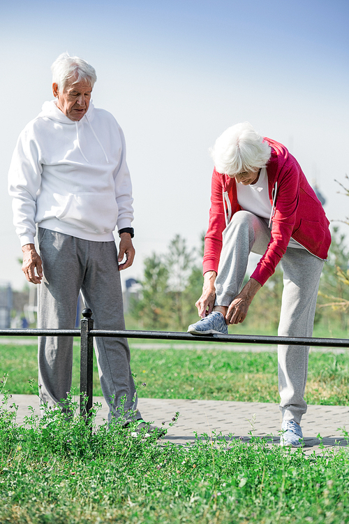 Full length portrait of active senior couple stopping to tie shoes during morning walk outdoors