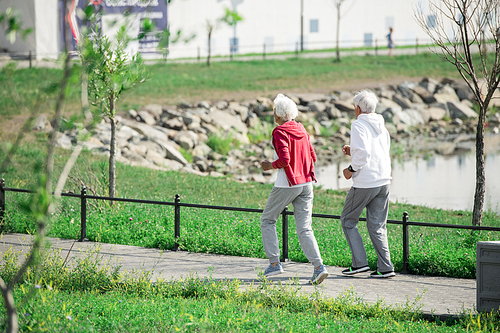 Full length portrait of active senior couple running outdoors in park along lake, copy space