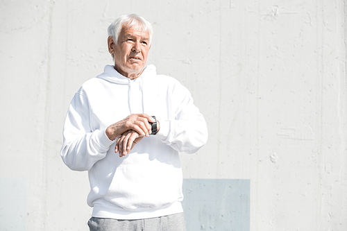 Waist up portrait of modern senior man setting up smart watch and looking away while doing morning run in park, copy space