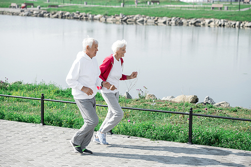 Full length wide angle portrait of senior couple running together in park along lake in sunlight, copy space