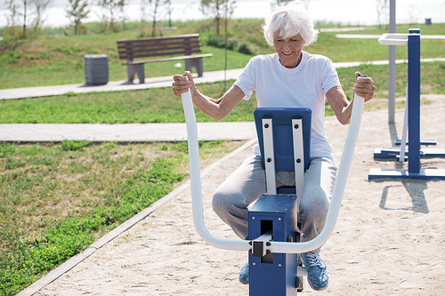 Full length portrait of smiling senior woman using outdoor exercise machines and enjoying workout, copy space