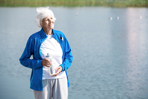 Waist up portrait of active senior woman looking away  and holding water bottle while enjoying morning run in park, copy space